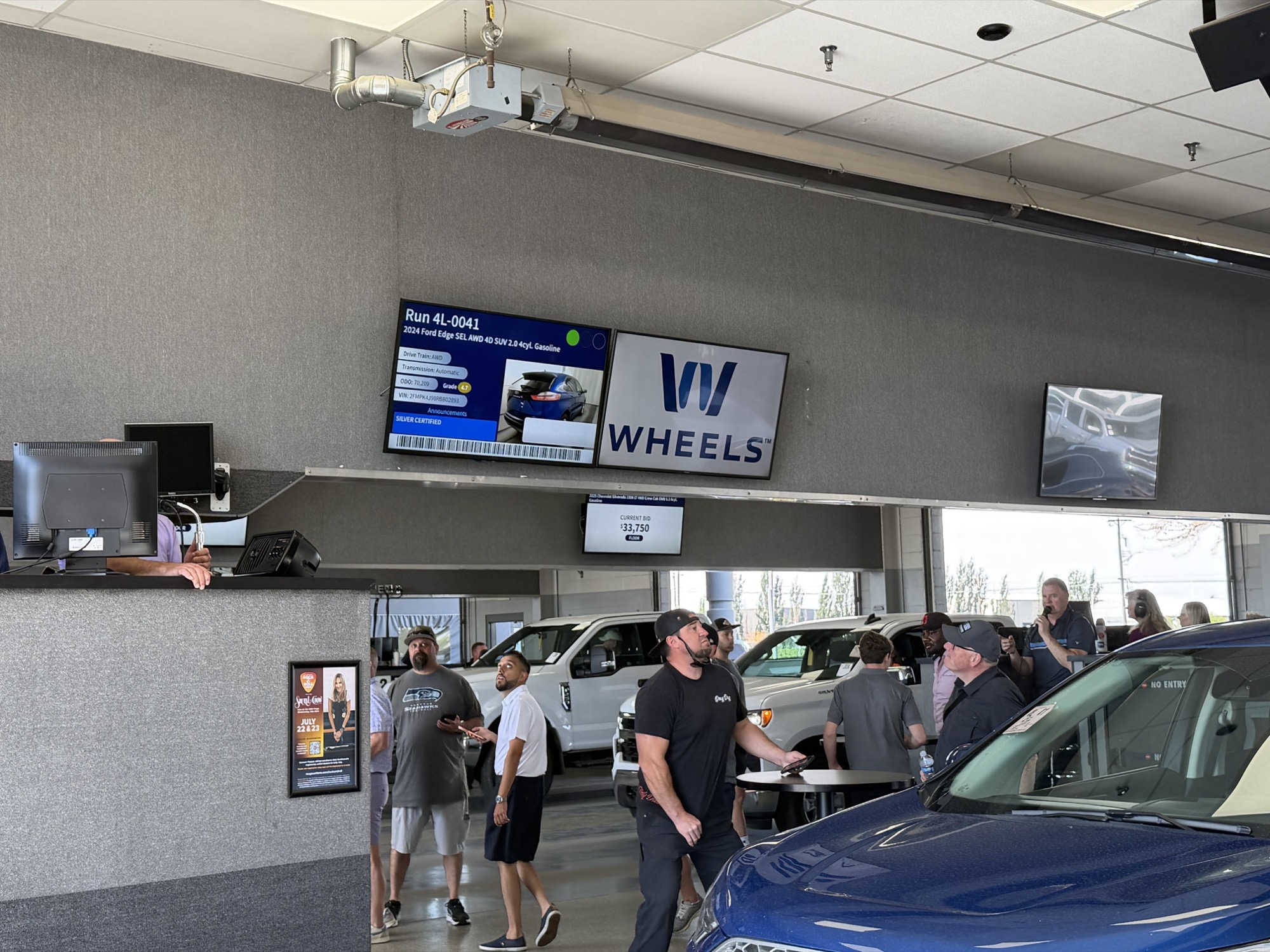 A Wheels consignor logo displayed beside the vehicle information screen in a live MAG auction lane